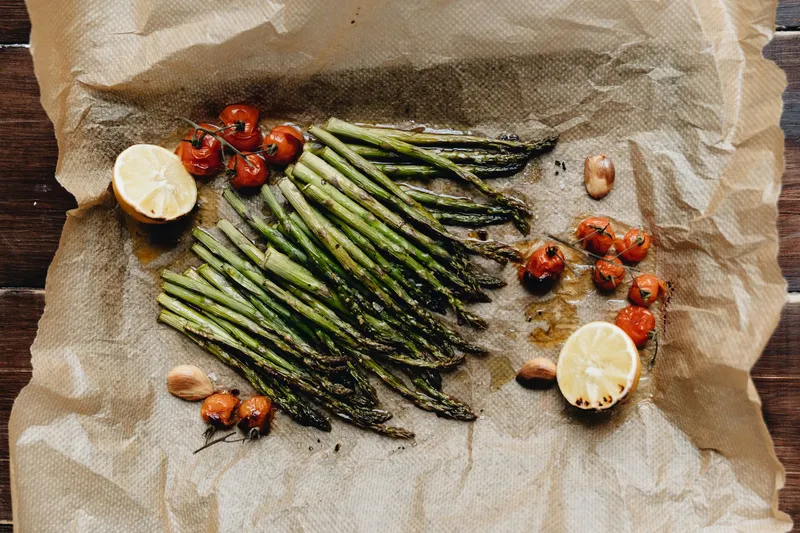Gebackener grüner Spargel mit Cherrytomaten, Zitronenhälften und Knoblauch auf Backpapier